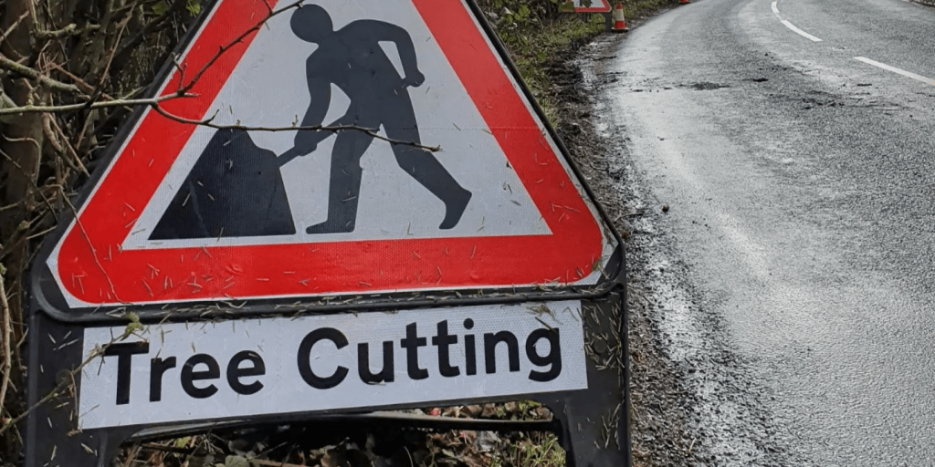 Warning triangle sign with tree cutting text printed and placed next to road where work tree surgery work is ongoing.